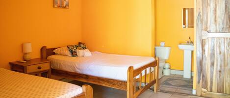 Una habitación con cama, mesita de noche, una pequeña mesa y baño con inodoro y lavamanos.