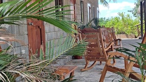 A covered outdoor area with a concrete floor, wooden benches, and potted plants.