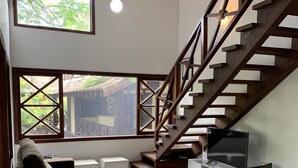 Una sala de estar moderna con una escalera, ventanas amplias y un televisor de pantalla plana.
