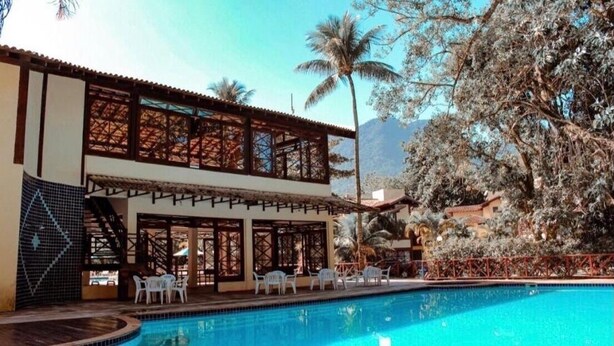 Un edificio de dos plantas con piscina, mobiliario exterior y palmeras.
