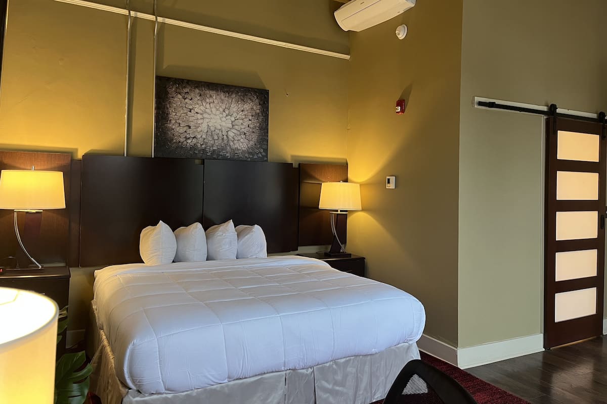 A hotel room with a large bed, two bedside lamps, a ceiling fan, and a wall-mounted air conditioner.