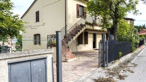 A two-story building with a staircase leading to a balcony, a gated entrance, and a paved pathway. - A28 - Poggio, large three-room apartment with porch (Poggio)