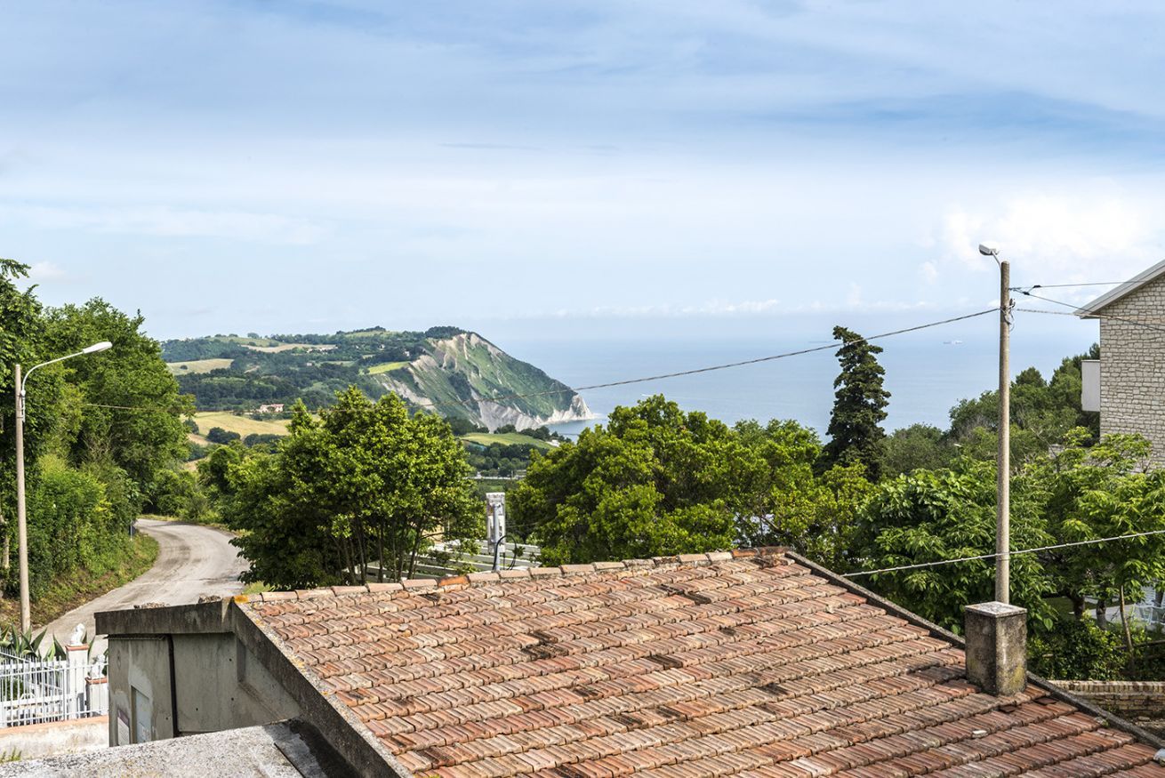 A rooftop with a view of a coastal landscape, including a hill and the sea.