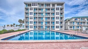 Um hotel com vários andares, piscina, área de estar externa e placa de aviso com salva-vidas.