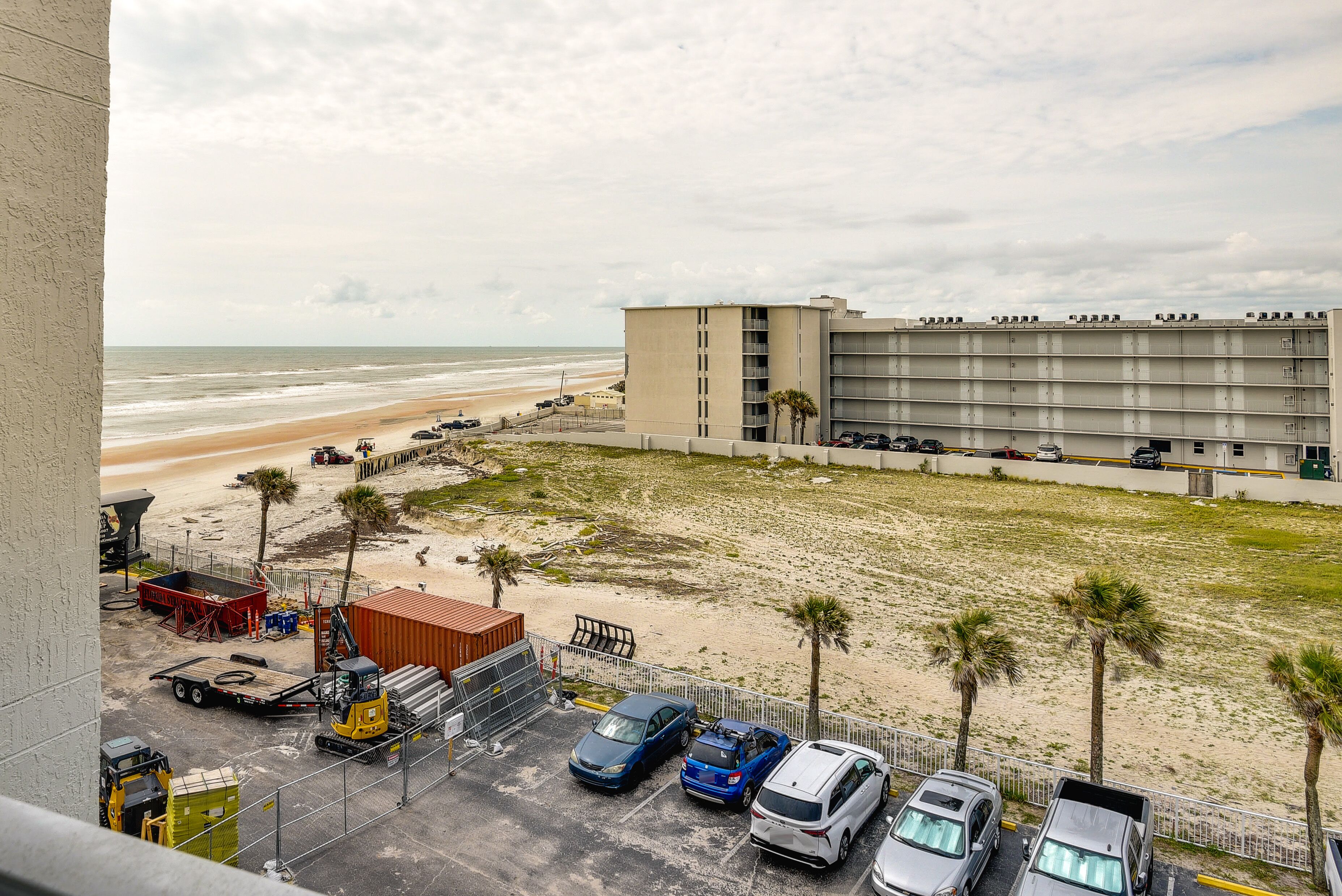 Un'area di parcheggio con diverse auto, un edificio a più piani e una spiaggia sullo sfondo.