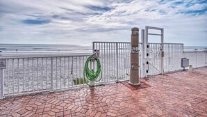 Uma passarela pavimentada com guarda-corpo de metal, uma mangueira verde e um portão que dá para uma praia.