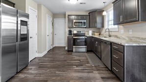 Une cuisine moderne dotée d’appareils électroménagers en acier inoxydable, de meubles de rangement aux couleurs sombres et d’un parquet en bois disposé en chevrons.