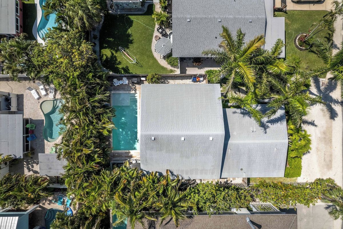 An aerial view of a residential property with a swimming pool, a covered patio, and a lawn with palm trees.