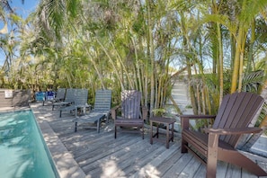 A wooden deck with lounge chairs and a pool, surrounded by palm trees.