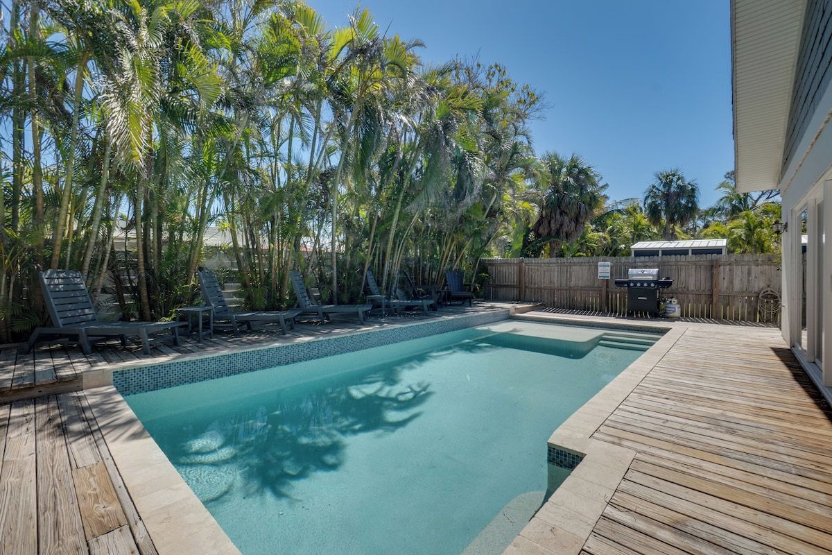 A swimming pool with a wooden deck, surrounded by palm trees and lounge chairs.