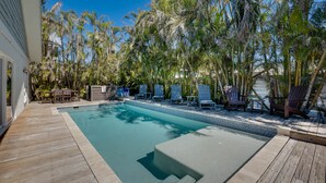Una piscina rectangular con muelle de madera, bordeada por sillas de descanso y una pequeña mesa.