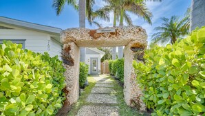 Un sendero conduce a una casa con un arco de piedra, rodeada de exuberante follaje verde.