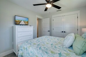 Quarto com cama, cômoda, ventilador de teto e televisão sobre a cômoda.