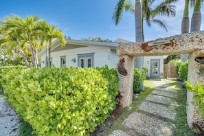 A white house with a stone archway, surrounded by lush greenery and palm trees. - Stonehenge (Anna Maria)