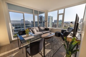 Una sala de estar moderna con una mesa de vidrio, un sofá gris y grandes ventanales con vistas a la ciudad.