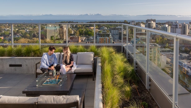 Terraza en la azotea con balaustrada de vidrio, mobiliario exterior y vistas a la ciudad y montañas.