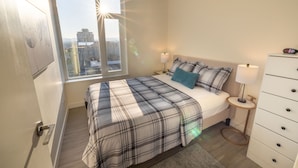 Un dormitorio con cama, mesita de noche, cómoda y ventana con vistas a la ciudad.