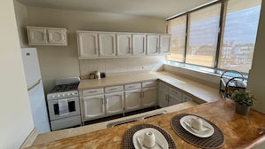 Una cocina con armarios blancos, estufa, refrigerador y ventana con vistas.