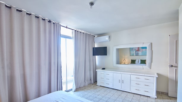 Una habitación de hotel con cama, televisor, cómoda y ventana con cortinas.