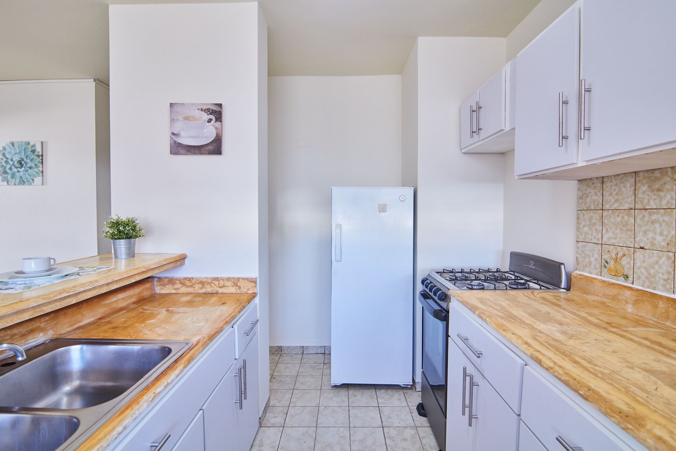 Une cuisine moderne avec des meubles blancs, un évier en acier inoxydable, un réfrigérateur et une cuisinière à gaz.