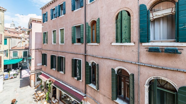 A multi-story building with arched windows and shutters, a visible storefront, and outdoor seating. - GuestHost - Apartment located on the first floor of a building, divided into two levels without a lift.In 85 square meters of space it comfortably accommodates four people with two bedrooms located on the second floor. There is an internal staircase.Loca (Venezia)
