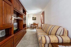 A living room with a sofa, wooden cabinets, a television, and a dining area with a table and chairs.