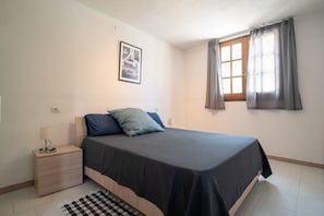 Een slaapkamer met een bed, nachtkastje, lamp en een raam met gordijnen.