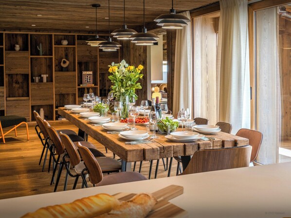 Een lange houten eettafel gedekt met borden, glazen en een bloemenstuk als decoratie.