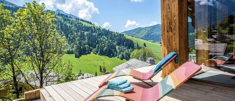 A wooden deck with lounge chairs and a view of a green valley and mountains.