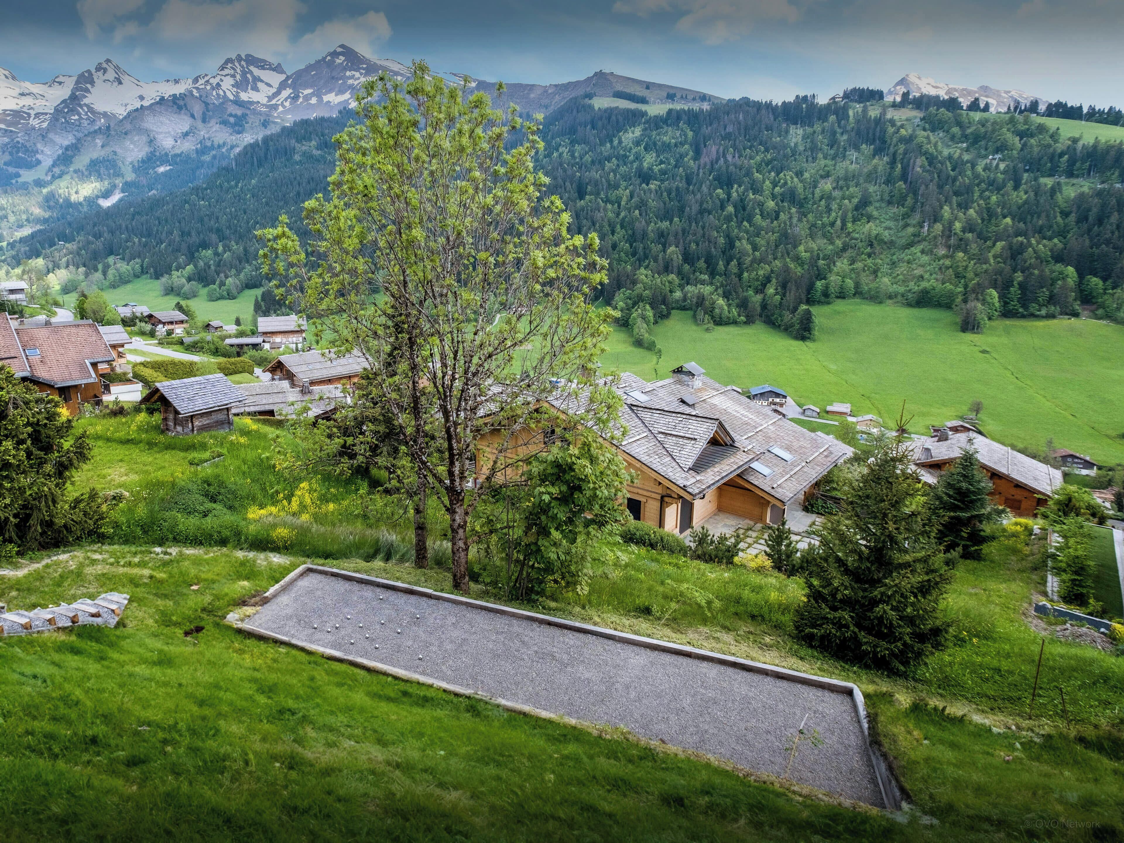 Un village rural avec des maisons traditionnelles en bois, une vue dégagée sur les montagnes environnantes et un espace verdoyant bien entretenu.