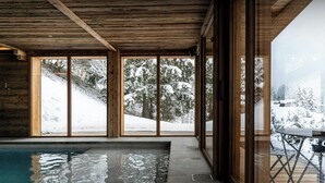 A modern indoor pool area with large windows offering views of a snowy landscape. - Chalet Arpitania - luxury chalet for 14 with pool and spa - OVO Network (La Clusaz)