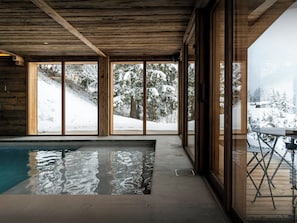 Un espace piscine intérieur moderne, doté de grandes fenêtres offrant une vue sur un paysage enneigé.