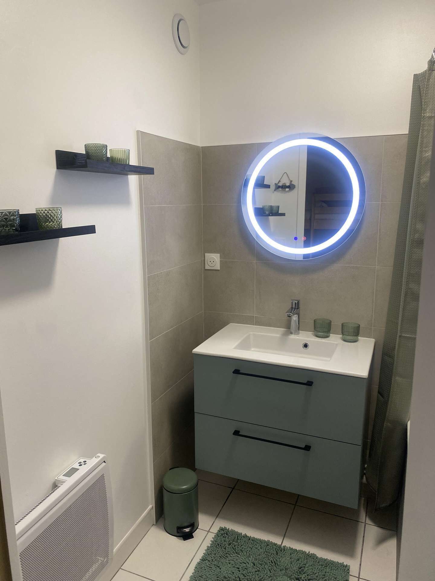 A small bathroom with a white sink, a mirror with a blue light, a heater, and a trash bin.