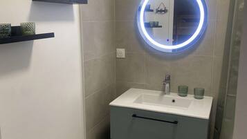 A small bathroom with a white sink, a mirror with a blue light, a heater, and a trash bin.