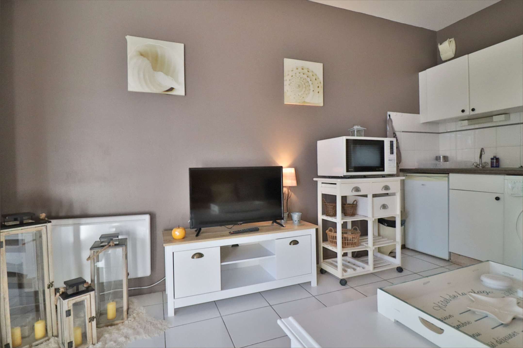Un soggiorno moderno con una televisione a schermo piatto, un mobile TV bianco, una piccola angolo cottura con un forno a microonde e un armadietto bianco.