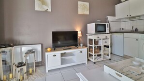 Un salon moderne doté d’un téléviseur à écran plat, d’un meuble de rangement blanc, d’un petit coin cuisine avec un micro-ondes et d’une armoire blanche.
