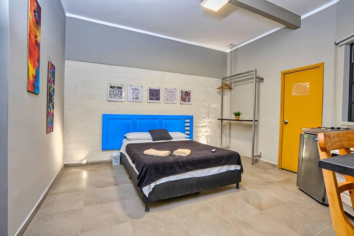 Une chambre à coucher moderne avec un lit, une tête de lit bleue, un petit bureau et une porte jaune.