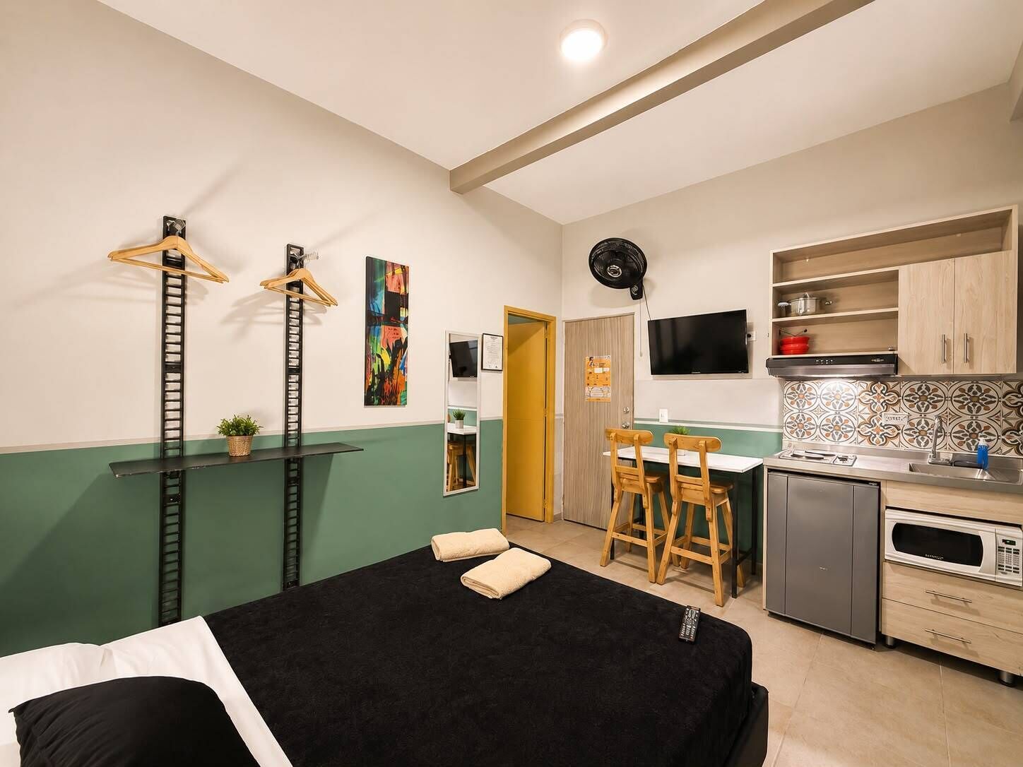 Una habitación compacta con cama, escritorio, kitchenette y televisor.