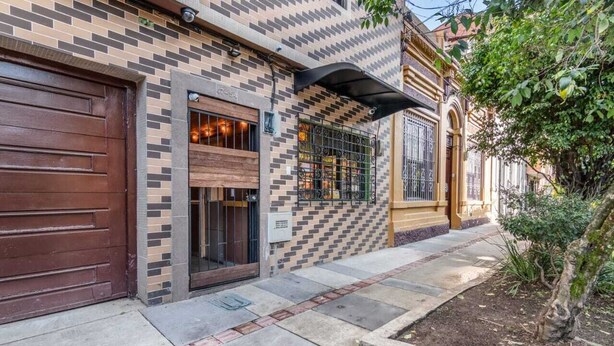 A building with a brick facade, a wooden garage door, and a small garden area with a tree. - La Gruta Co-Living  (Medellín)