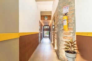 A corridor with a fire extinguisher mounted on a stone wall, a potted plant, and a sign indicating an exit.