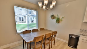 A dining area with a wooden table and chairs, a window with blinds, a wall-mounted plant, and a trash can. - 227 - Bear Lake Escapes. Beautiful Home in an Unbeatable Location (Garden City)