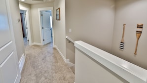 A hallway with beige walls, white trim, and a carpeted floor. There are wooden utensils hanging on the wall and a door leading to another room. - 227 - Bear Lake Escapes. Beautiful Home in an Unbeatable Location (Garden City)