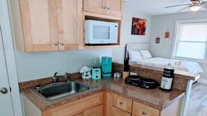 A compact kitchen with wooden cabinets, a built-in microwave, a sink, and a countertop with various appliances. - Peaceful Studio Apt in Cental MB (Myrtle Beach)