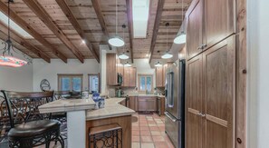 A kitchen with wooden cabinets, a stainless steel refrigerator, and a dining area with a table and chairs. - Valley View Lodge | Scenic Ruidoso Retreat w/ Hot Tub, Vaulted Ceilings & Valley Views (Ruidoso)