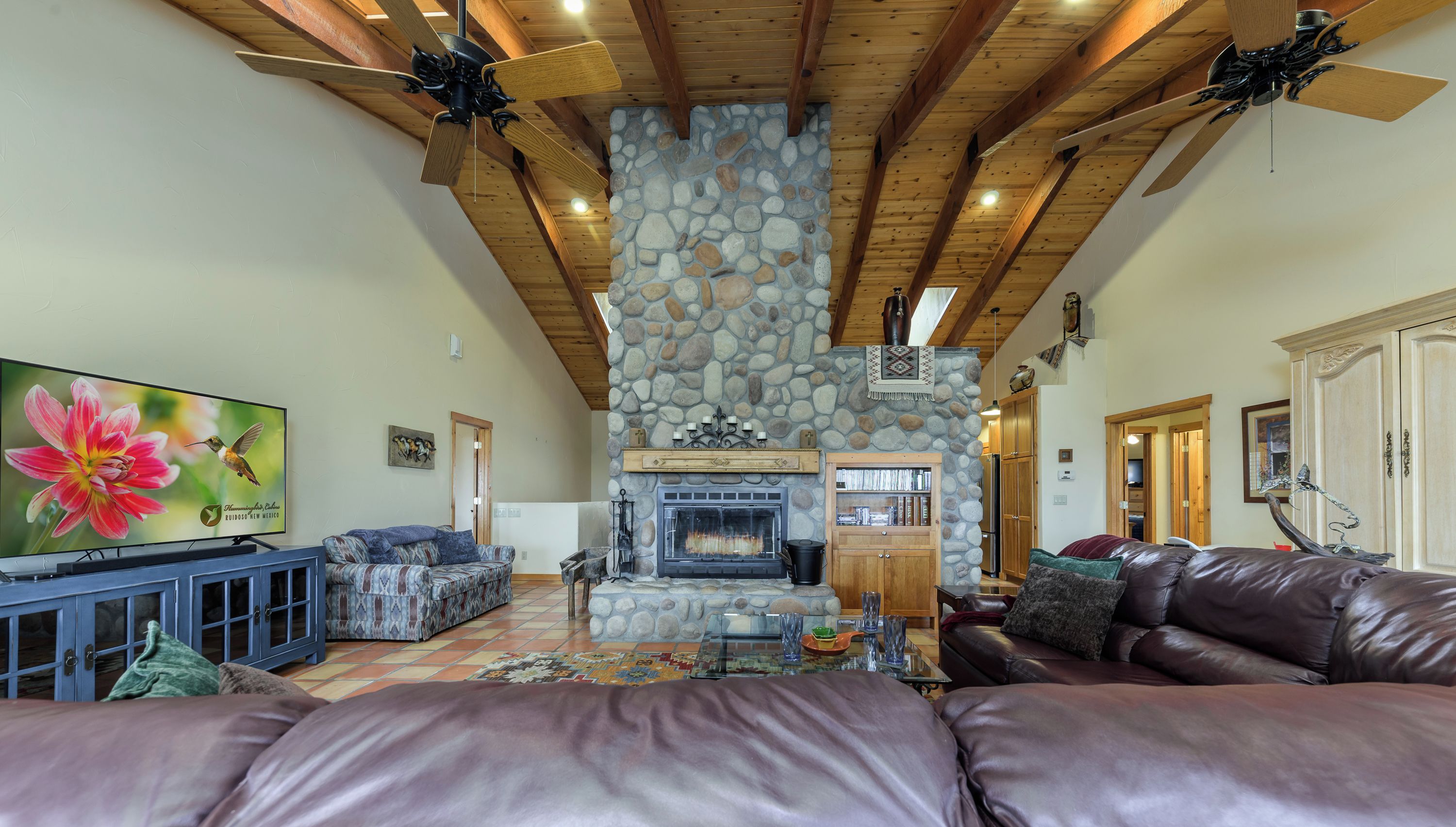 A spacious living room with a stone fireplace, leather furniture, and a television displaying a floral image.
