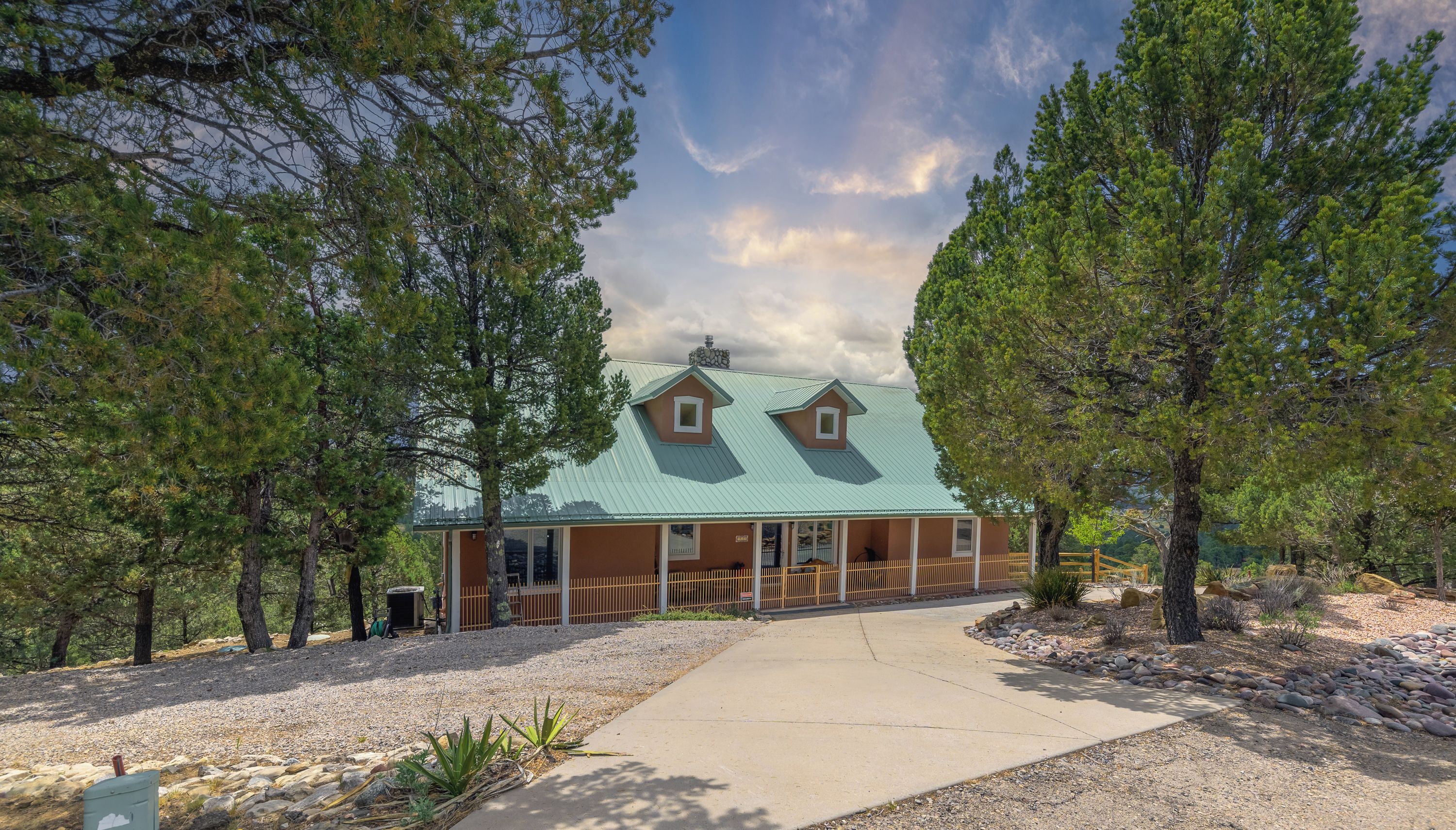 A cabin with a green roof, surrounded by trees, and a gravel driveway.