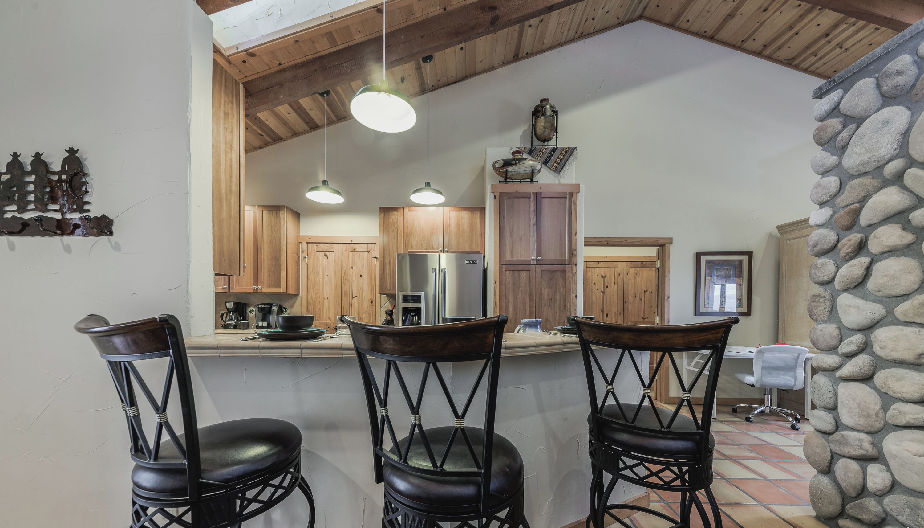 A kitchen with wooden cabinets, a refrigerator, and three black bar stools.