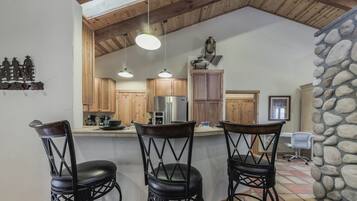 A kitchen with wooden cabinets, a refrigerator, and three black bar stools.