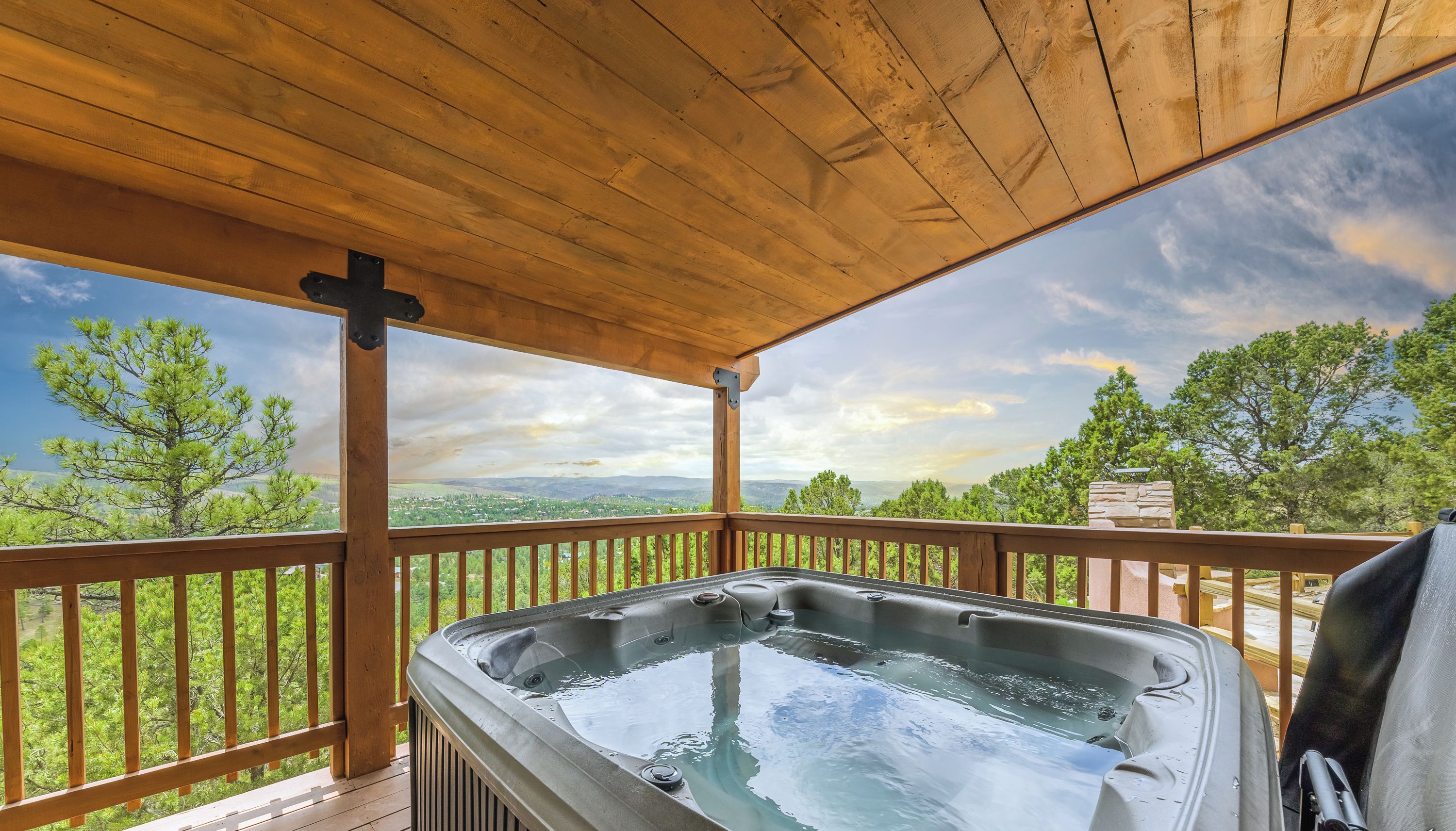 A hot tub on a wooden deck with a view of trees and mountains.