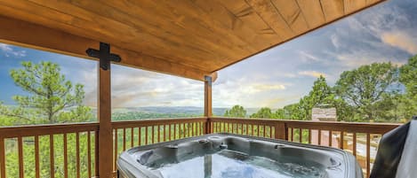 A hot tub on a wooden deck with a view of trees and mountains.